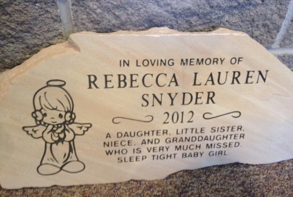 Flat stone marker memorial for embedded in brick wall with engraved angel design and personalized inscription.
