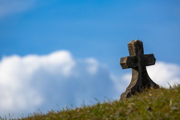Granite cross-shaped tombstone outdoors on grassy hillside beneath clouds