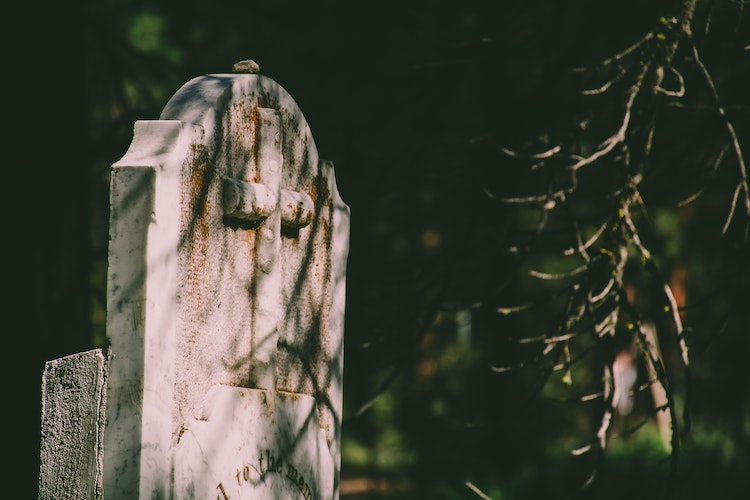 Granite tombstone with dirt and mossy growth on front surface