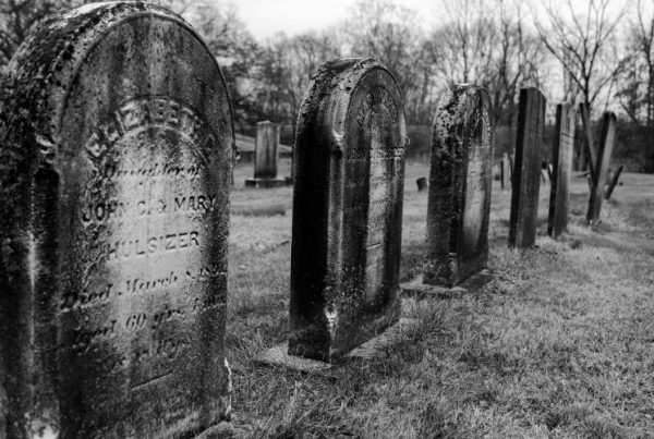 Black and white photo of older tombstones with surface damage and engraved inscriptions in graveyard